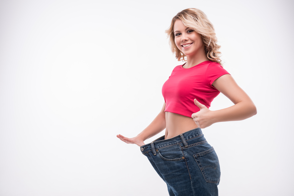 A woman happily posing with oversized jeans after significant weight loss using tirzepatide.