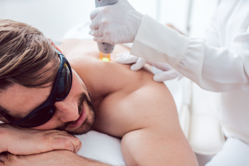 Man receiving laser hair removal treatment on his back at a clinic.