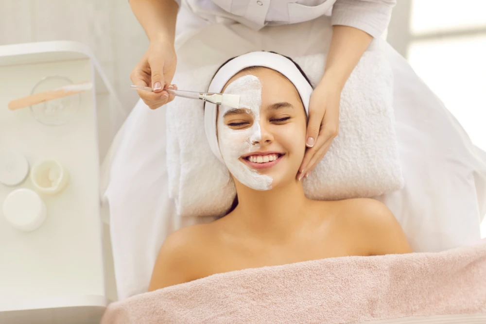 Smiling woman receiving a relaxing med spa facial treatment with a mask applied.