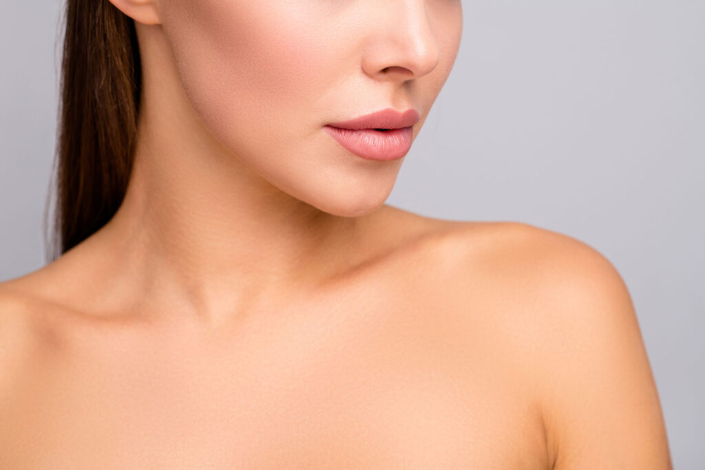 close-up of a woman’s lower face, lips, and neck with smooth skin against a gray background