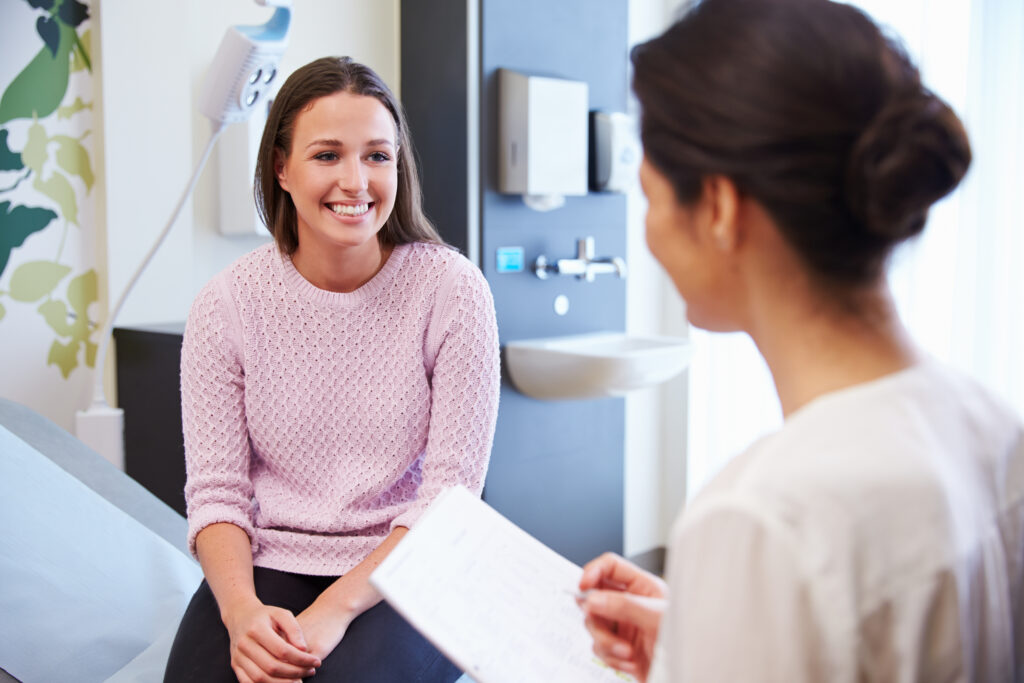 Two people seated in a medical exam room holding paperwork during a conversation