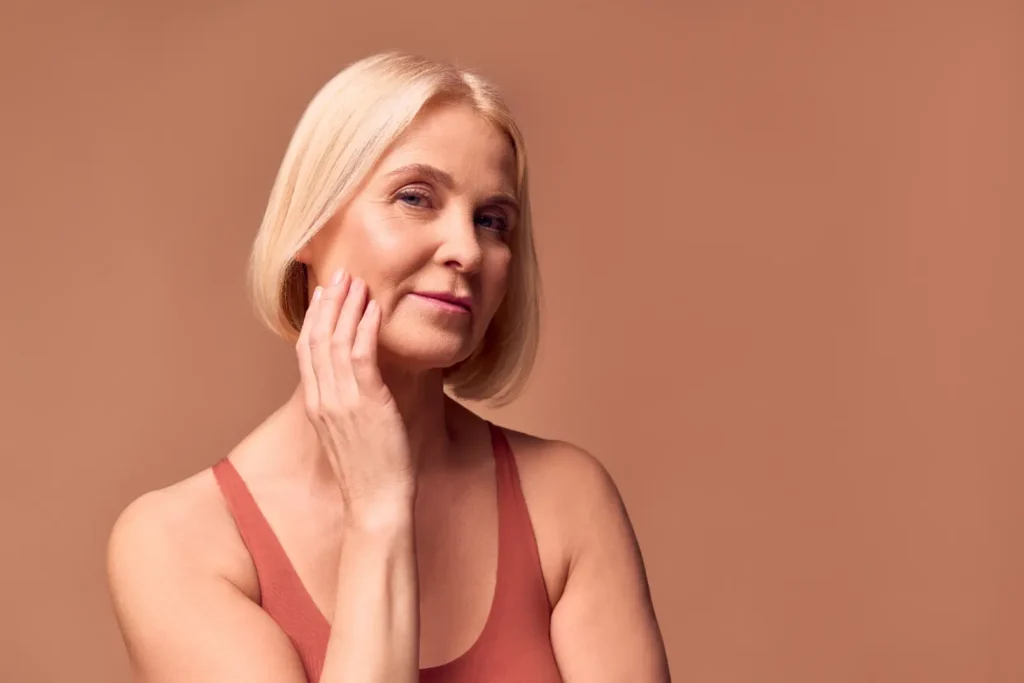Mature woman touching her cheek against a neutral background