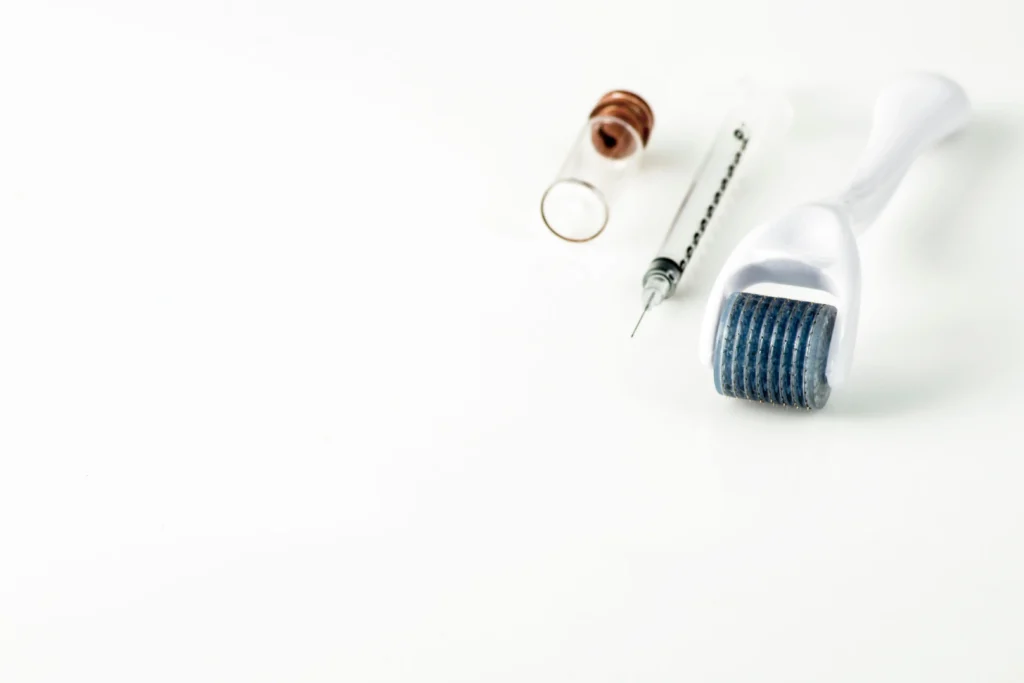 Syringe, vial, and microneedling roller arranged on white surface