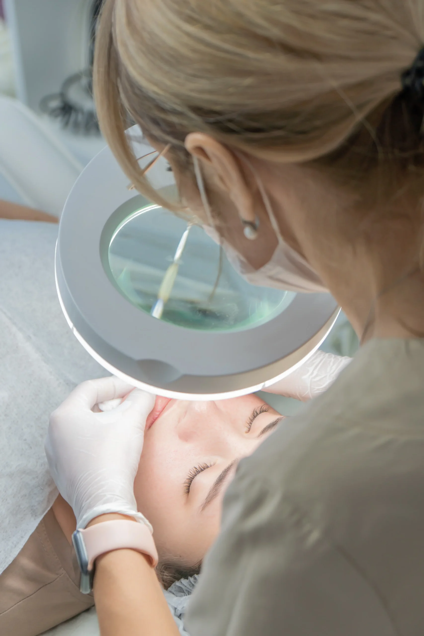 Practitioner using magnifying lamp while performing facial treatment on patient