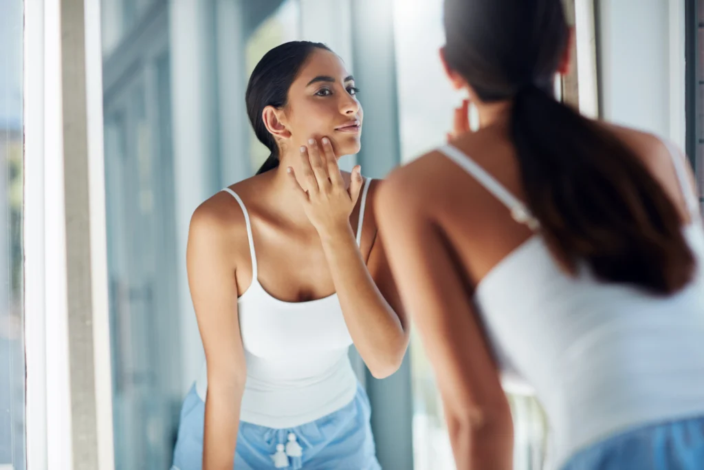 Woman touching face while looking in mirror during skincare routine