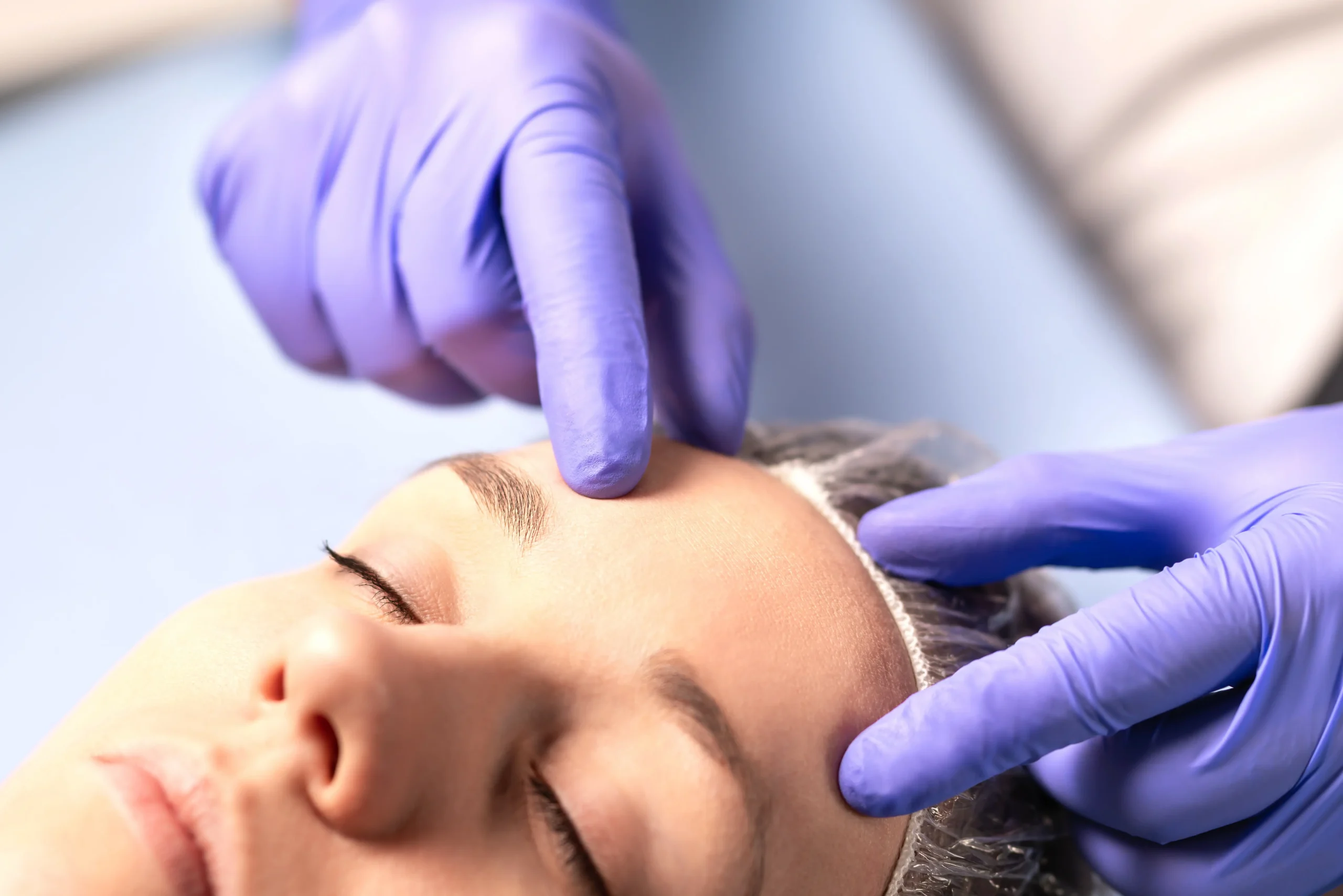 Gloved hands examining woman’s forehead during facial treatment
