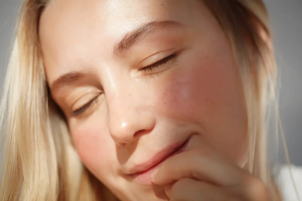 Close-up of a woman with smooth skin resting her hand near her chin in sunlight
