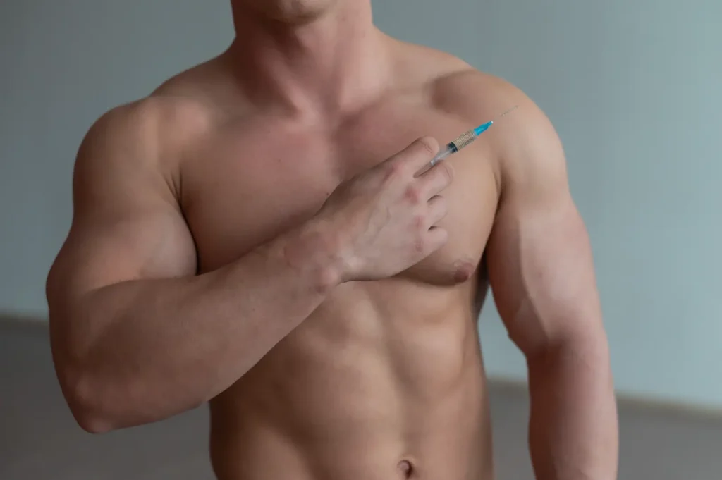 Shirtless man holding syringe near chest against neutral background