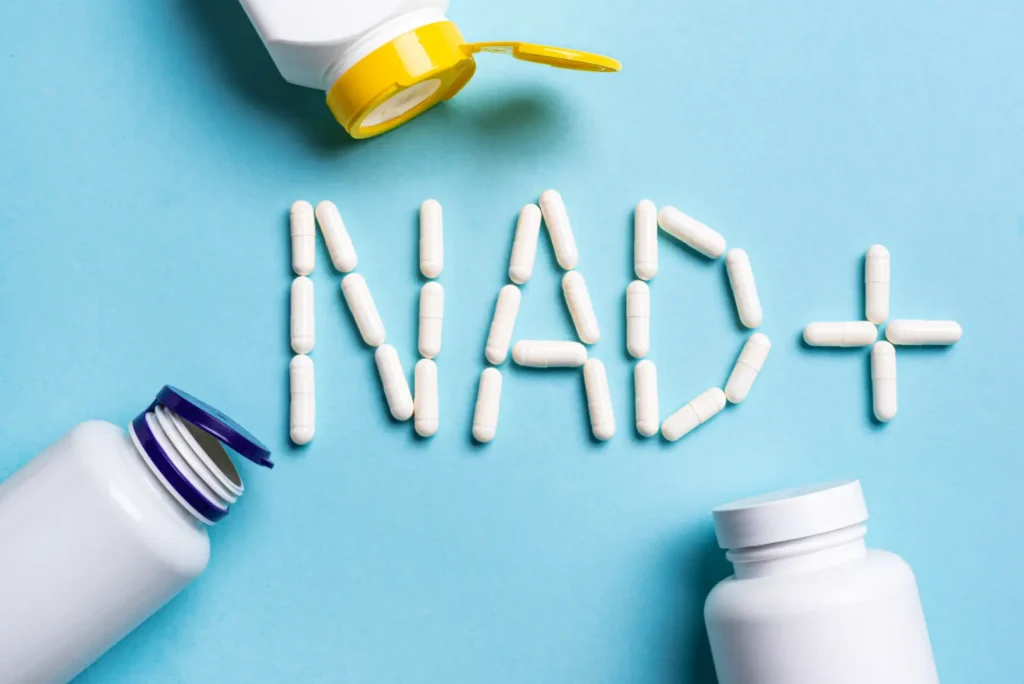 White capsules arranged to spell NAD+ beside supplement bottles on a blue surface